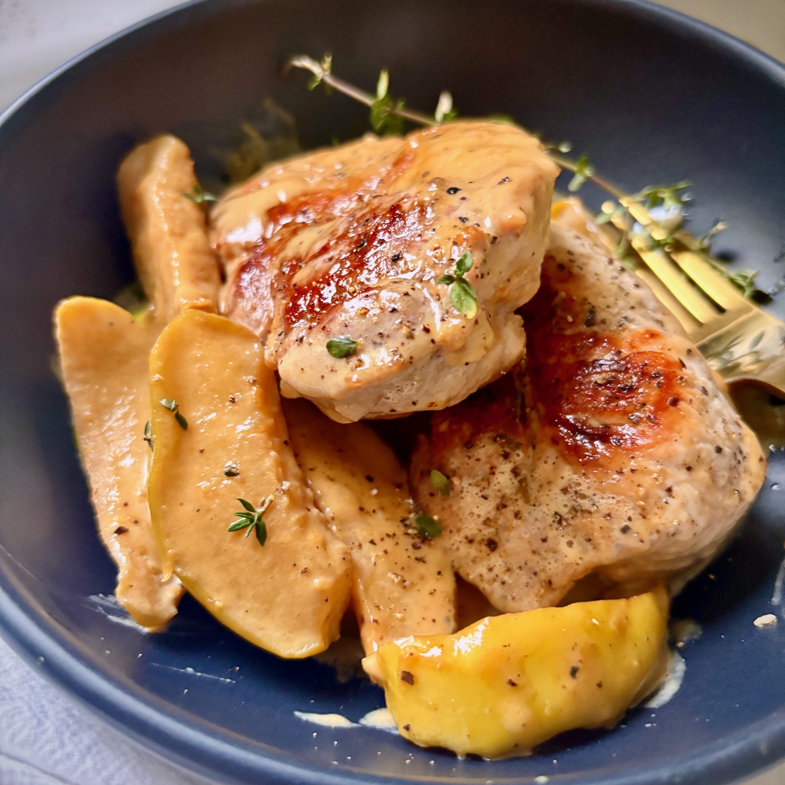 Plate of pork and apples drizzled with creamy miso maple sauce and thyme garnish