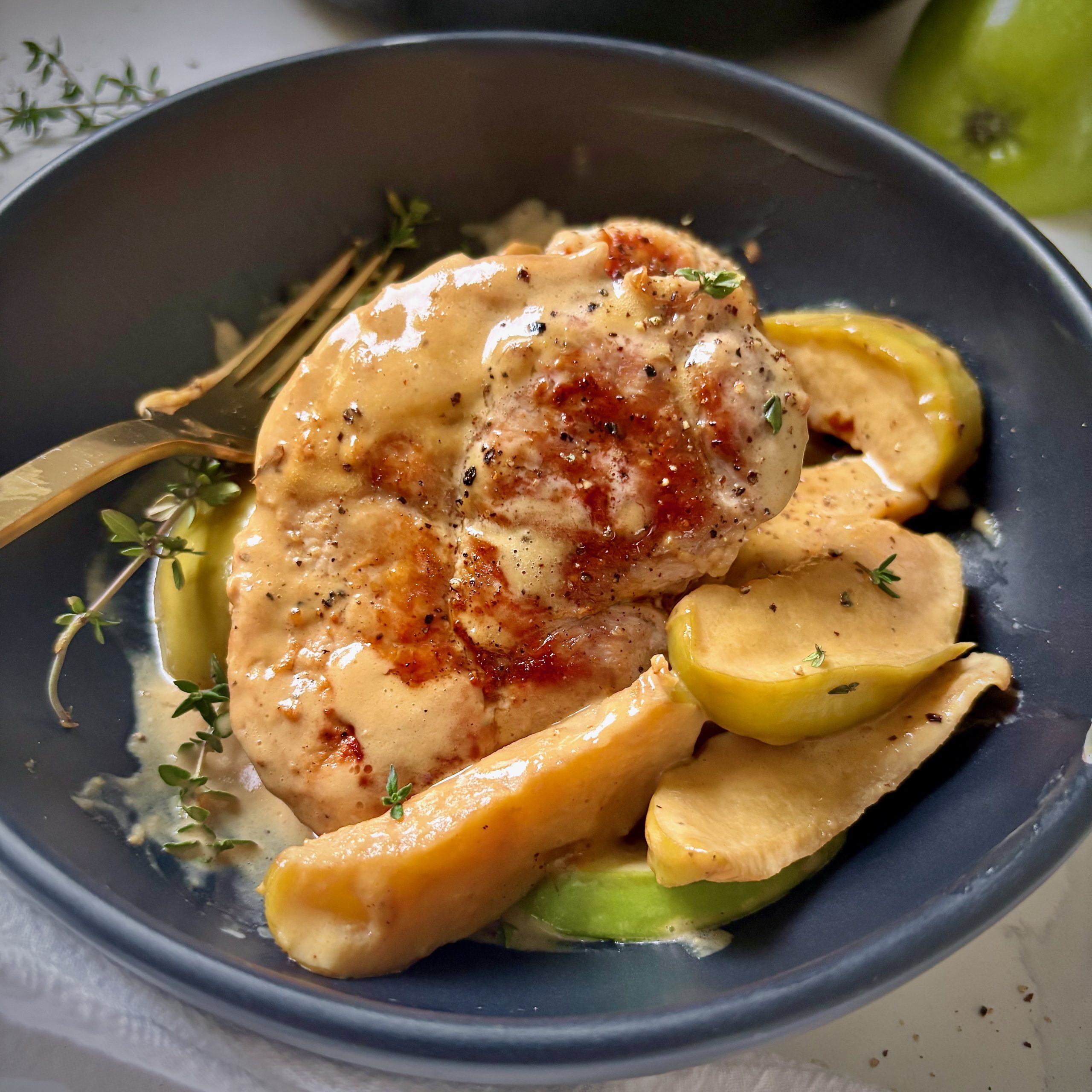 Dish of pork and apples served with creamy miso maple sauce and thyme garnish