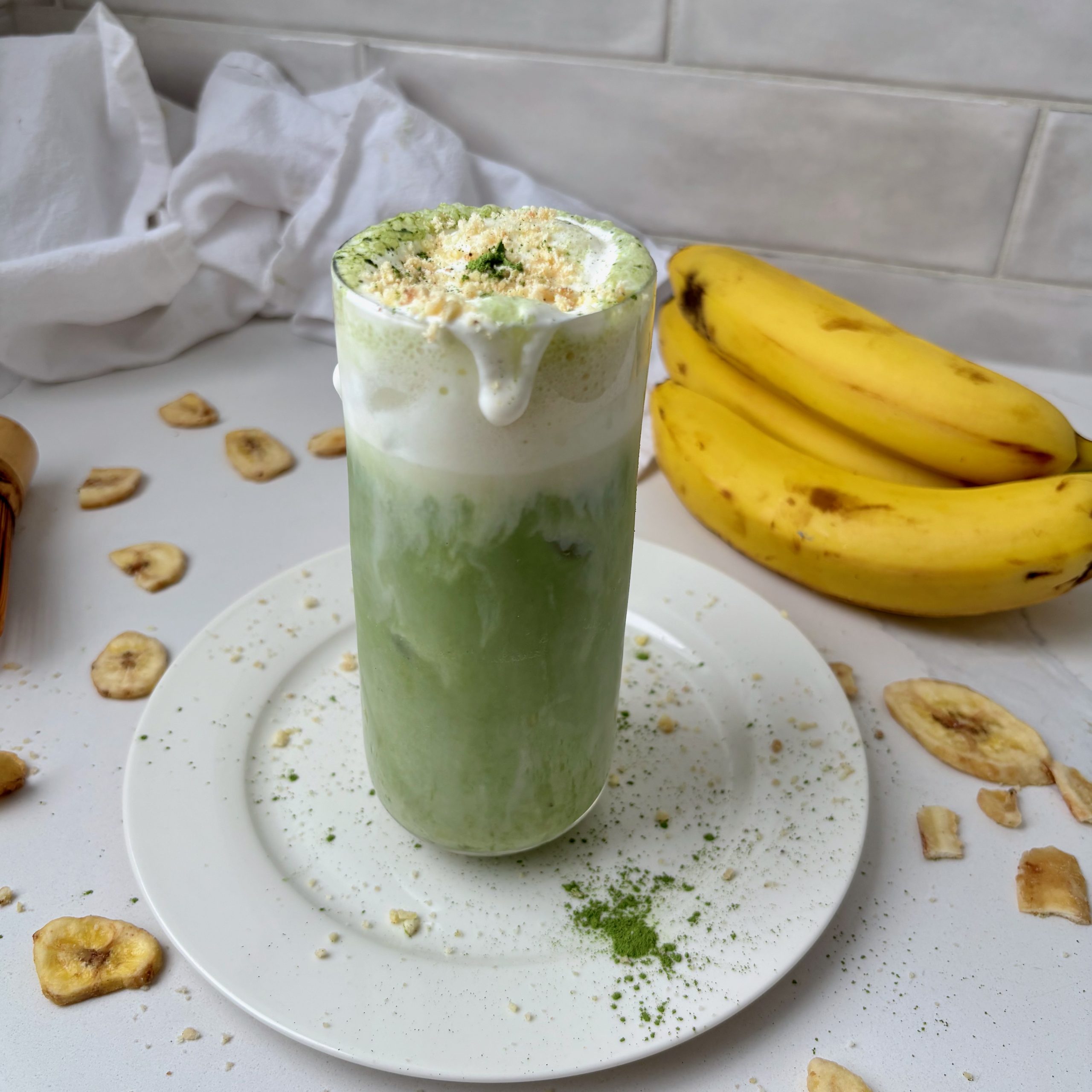 Banana Cream Matcha Latte in glass with bananas and banana chips