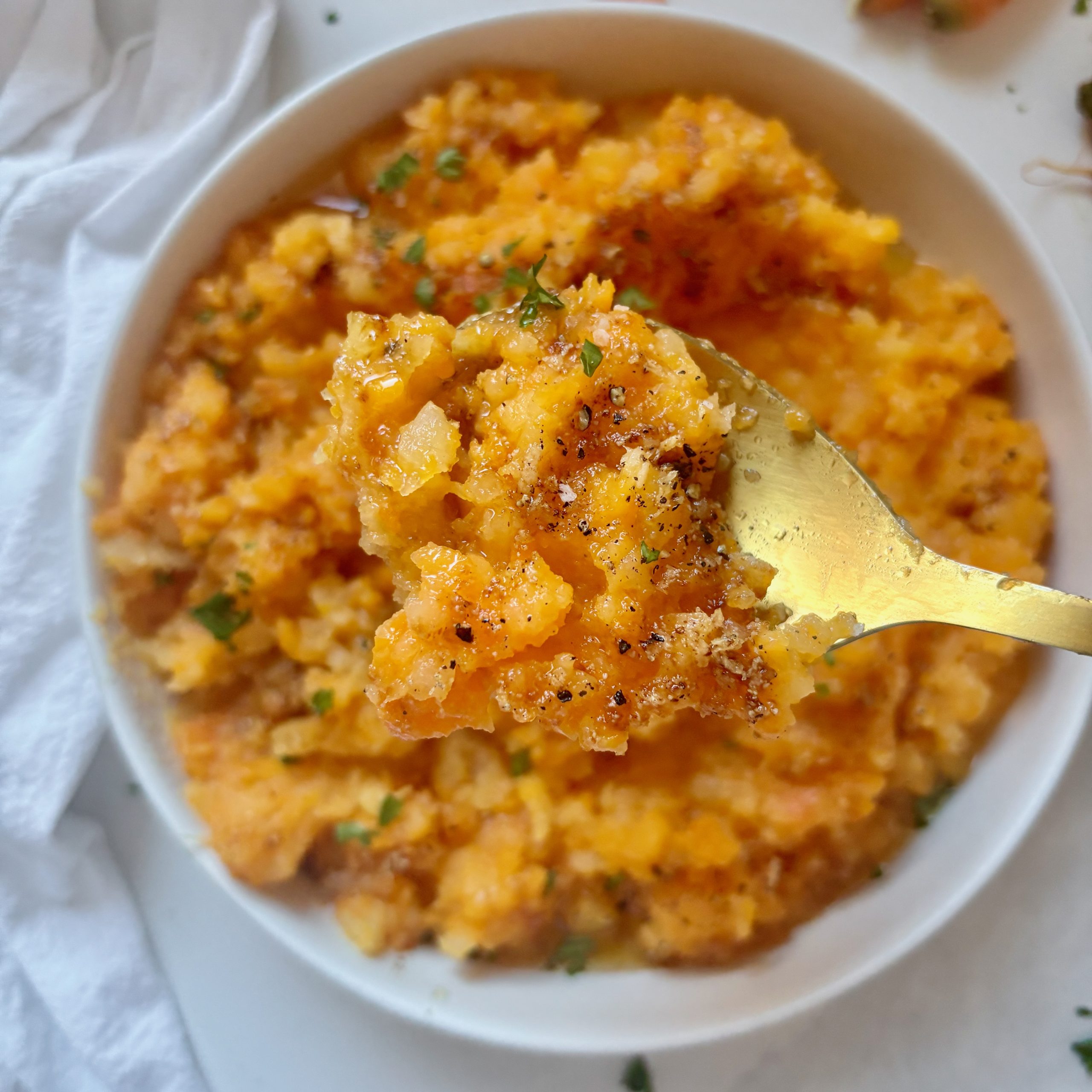 Close-up of rustic mashed carrots and rutabaga with visible browned butter and flecks of fresh parsley.