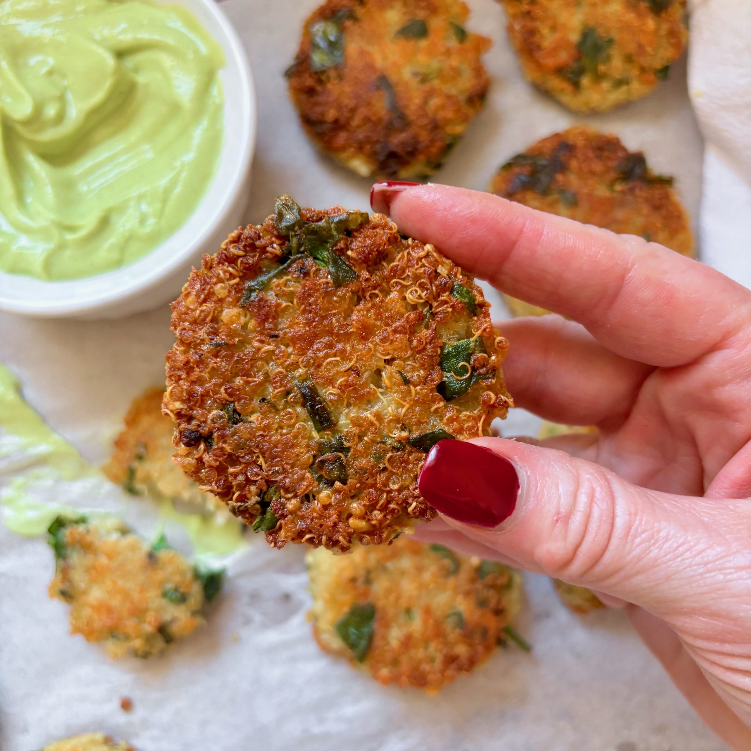 Close-up of golden cheesy quinoa bites with green dipping sauce