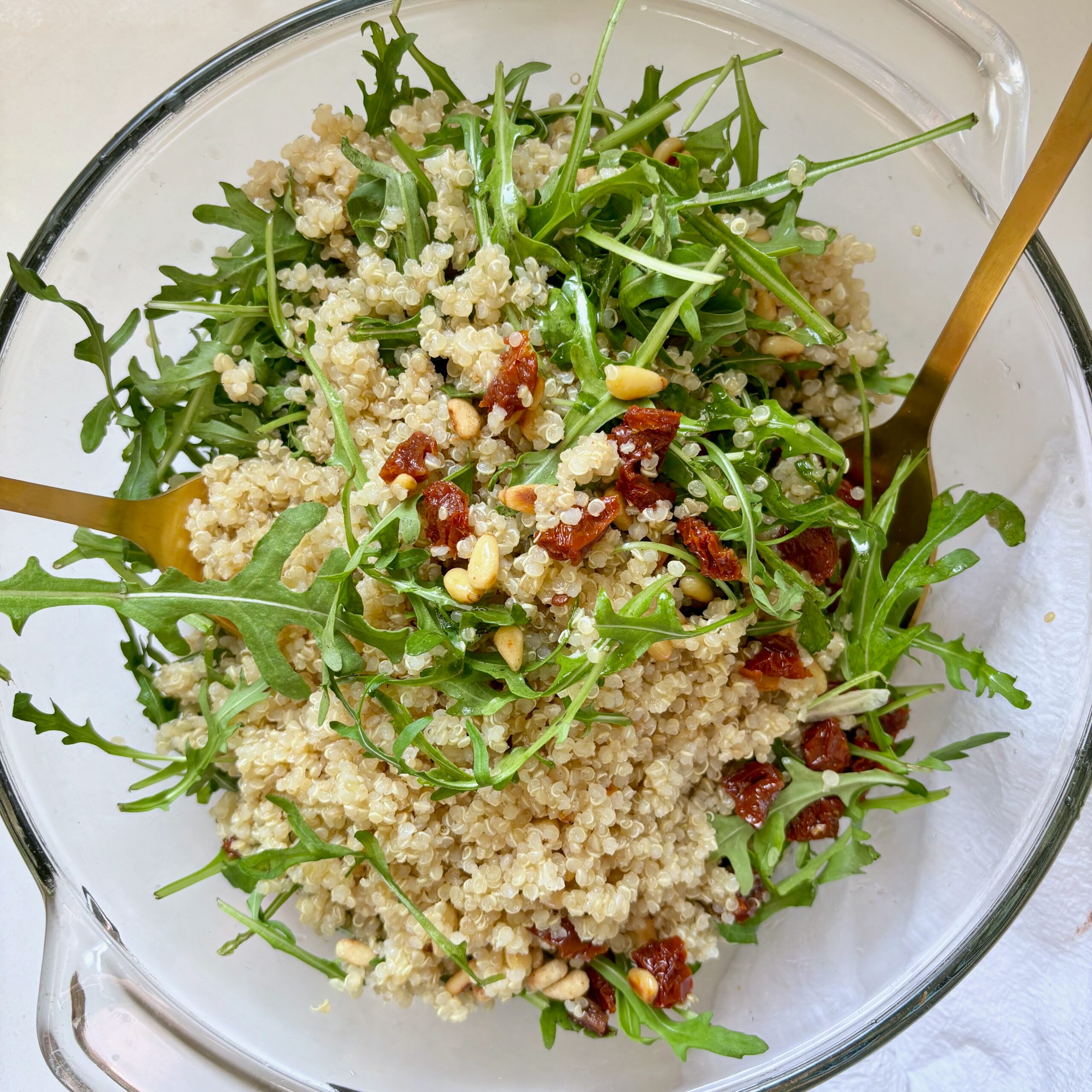 Quinoa arugula salad with pine nuts, sun-dried tomatoes, and parmesan in a large bowl