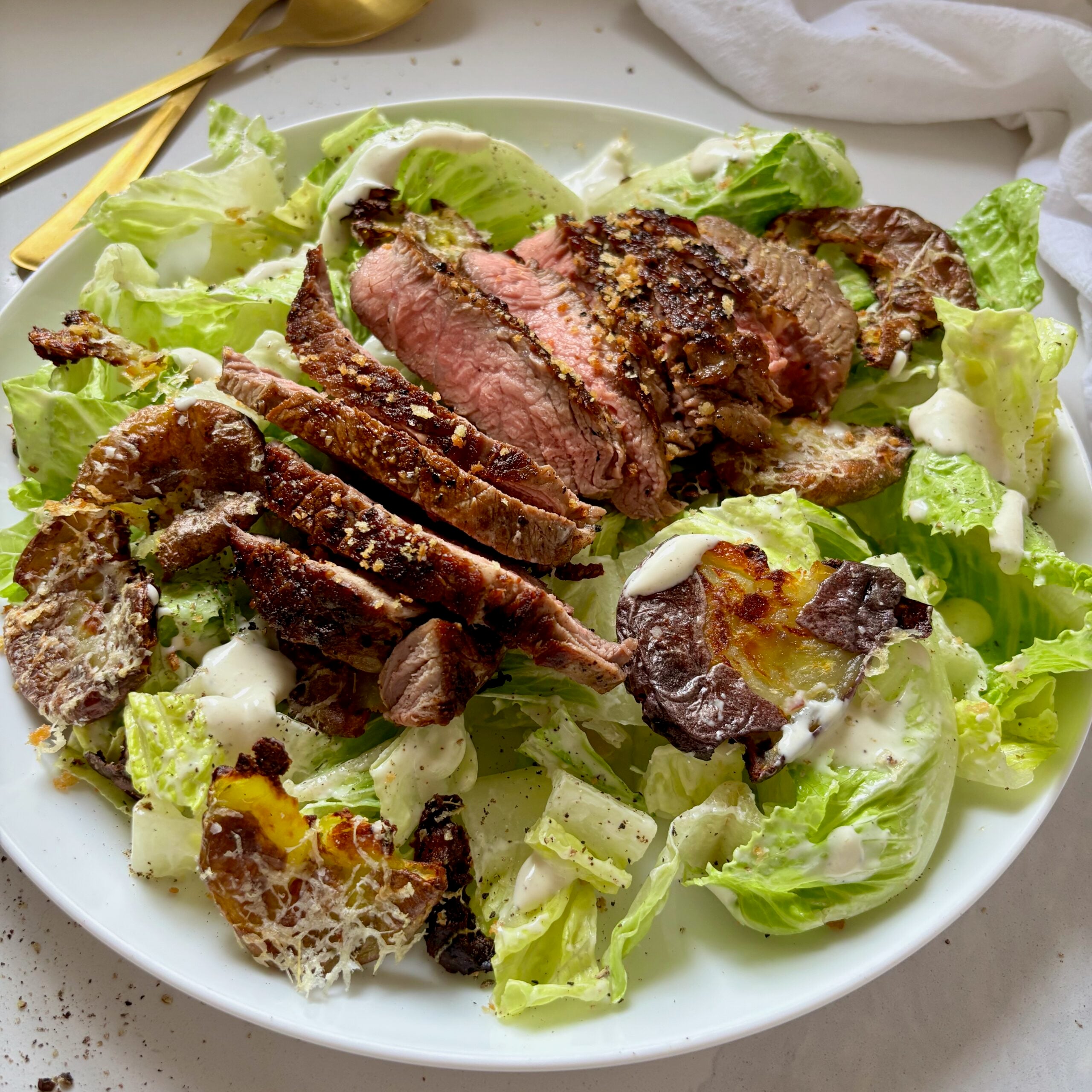 Caesar salad with sliced steak and crispy smashed potato croutons served in a large bowl.