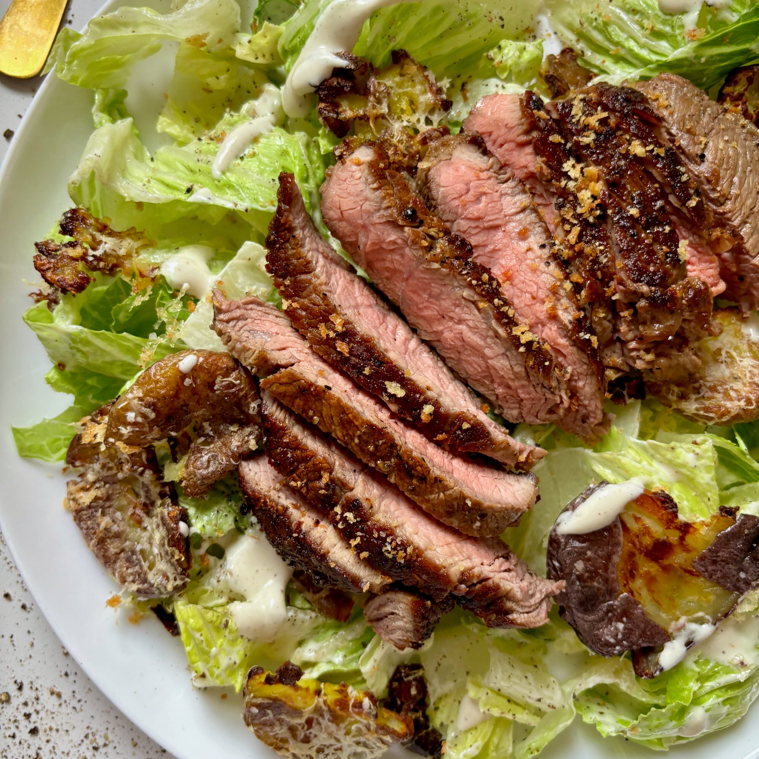 Close-up of Caesar salad topped with grilled steak, parmesan, and smashed potato croutons.