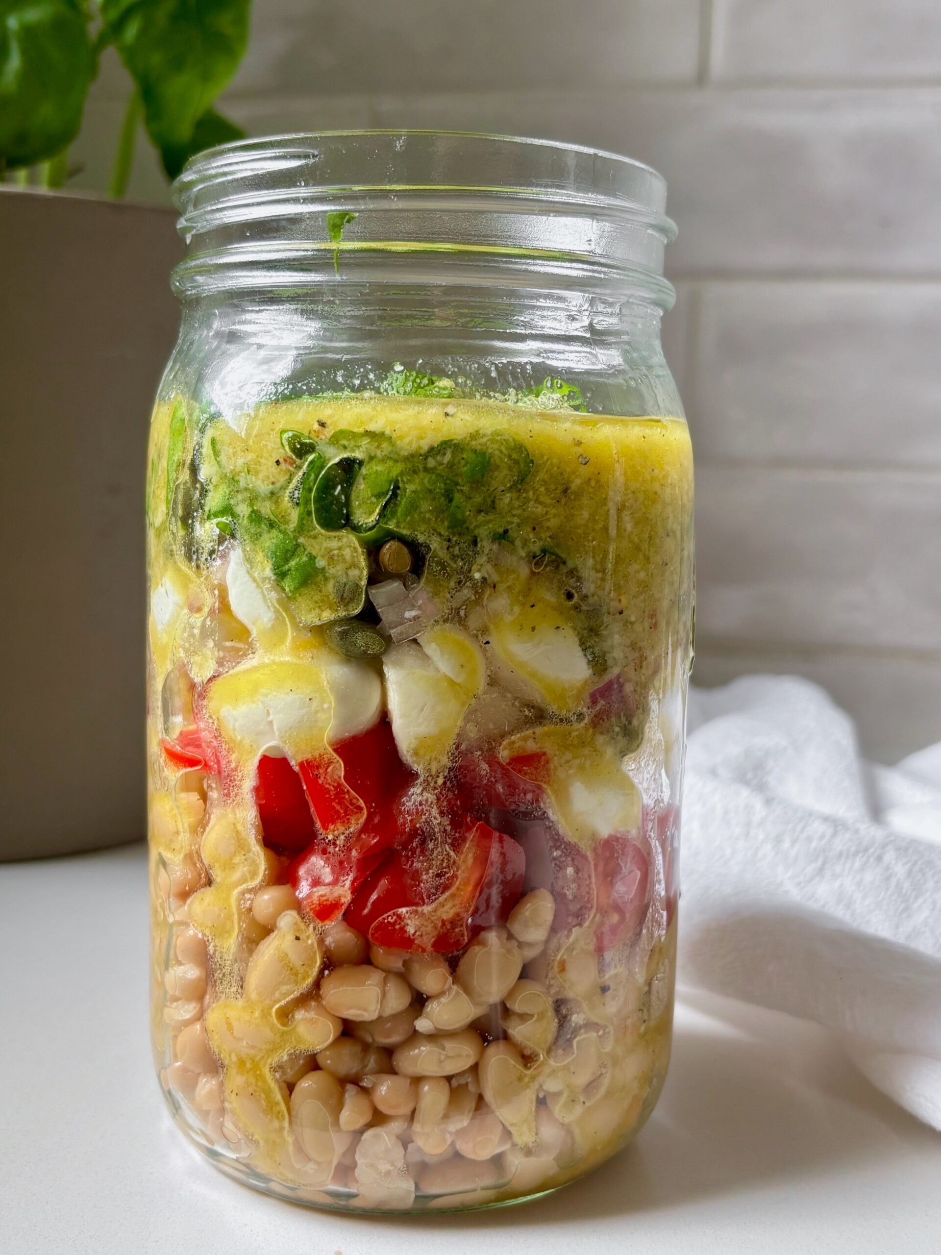 Glass jar filled with marinated white bean salad topped with fresh basil.