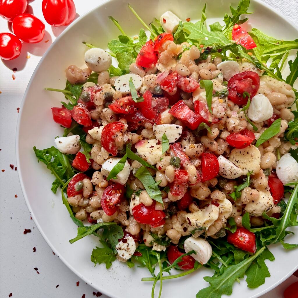 Close-up of white bean salad with tomatoes, basil, capers, and bocconcini.