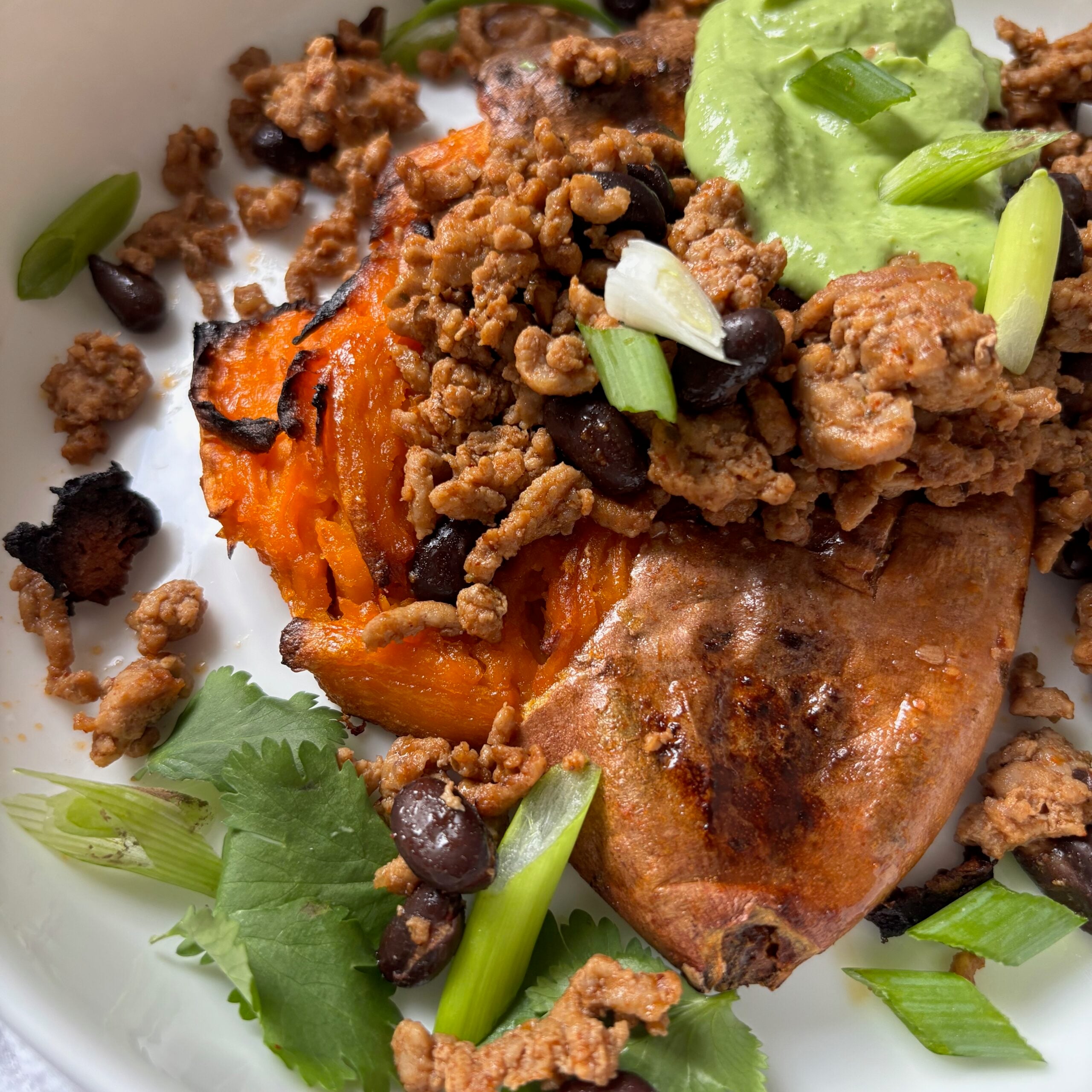 Crisp smashed sweet potato in a bowl loaded with ground turkey, black beans and creamy cilantro jalapeno sauce