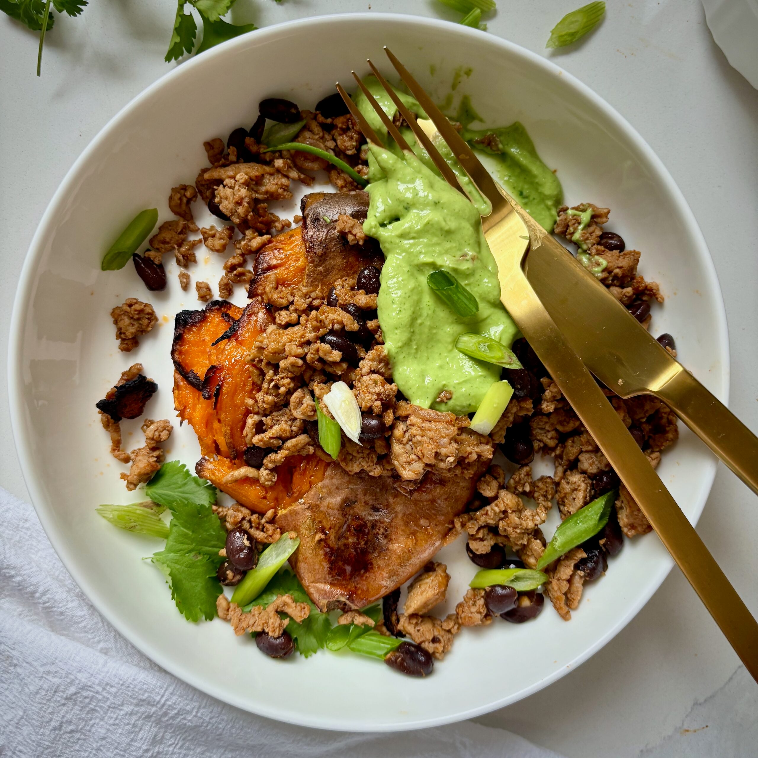 bowl with smashed and loaded sweet potato topped with creamy greek yogurt avocado sauce