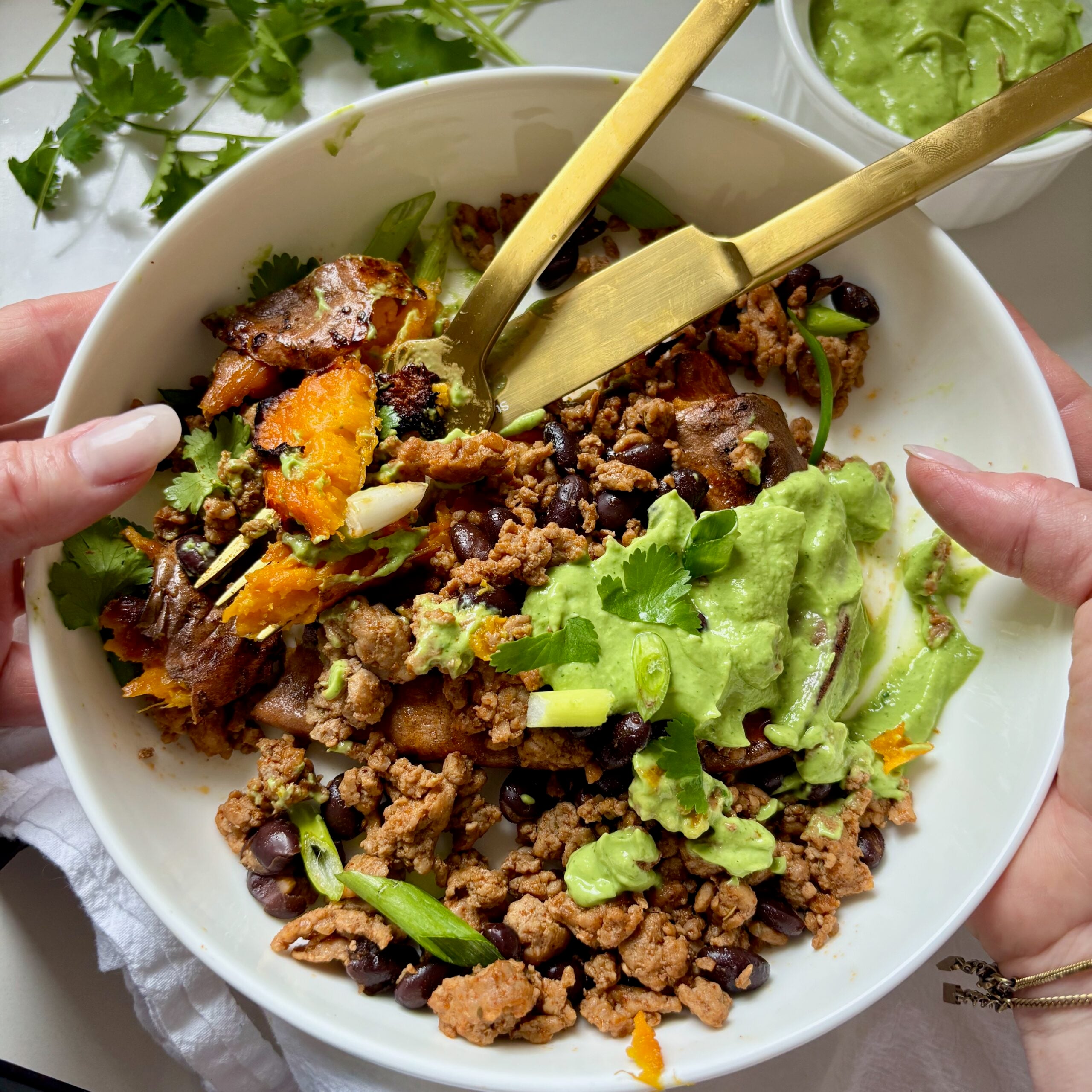 Bowl of smashed loaded sweet potato topped with ground turkey, black beans and creamy avocado jalapeno sauce