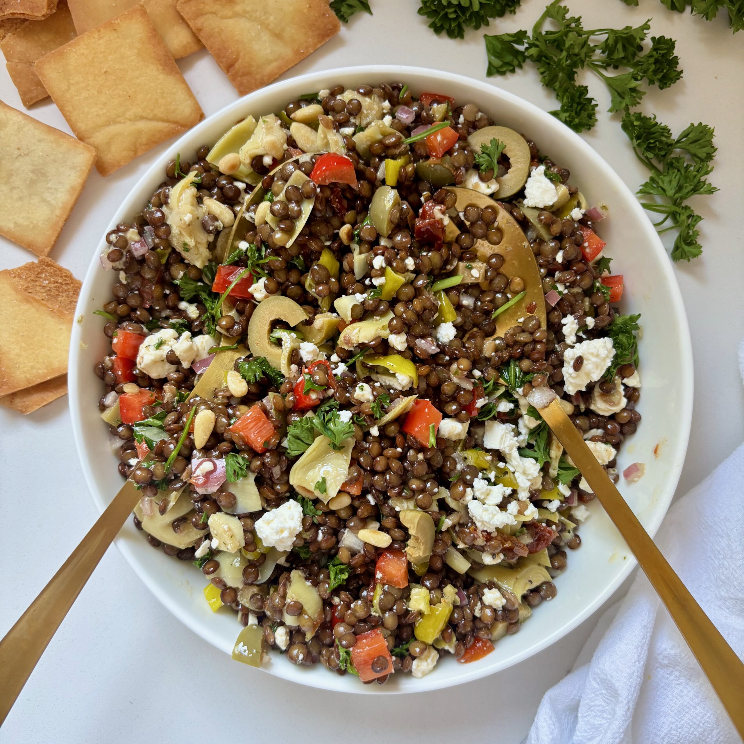 Mediterranean Marinated Lentil Jars poured into large bowl with serving spoons and pita chips