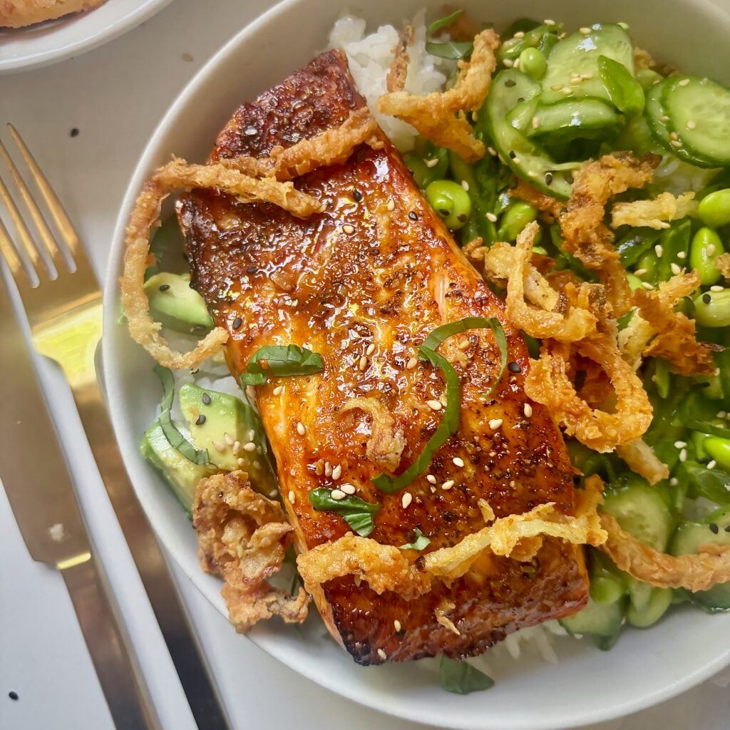 Close-up of mustard-glazed salmon served over rice with edamame and snap pea salad.