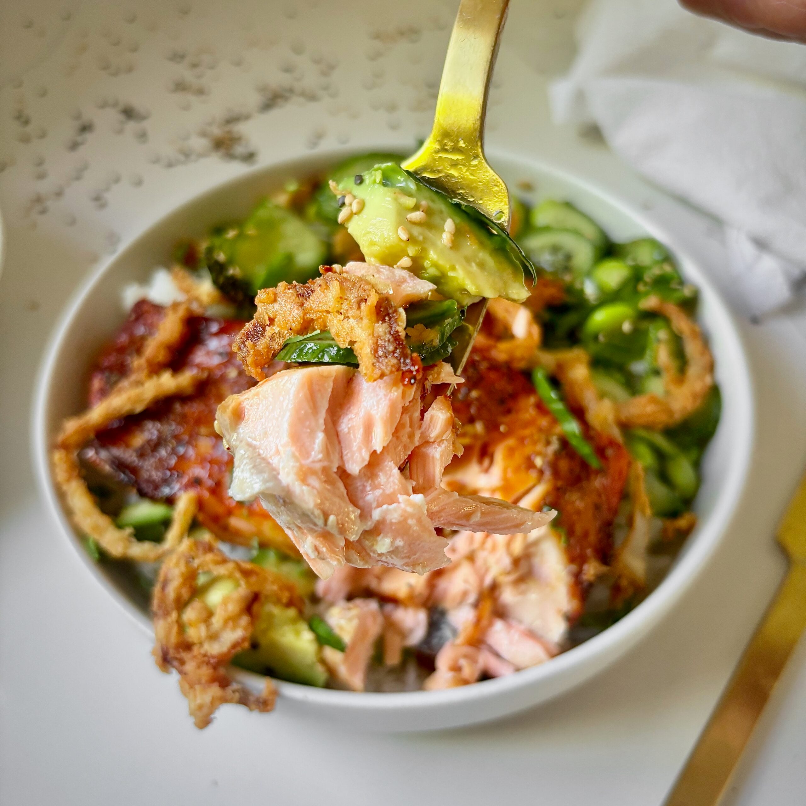 Fork lifting salmon, rice, avocado, and crunchy vegetables from a bowl.