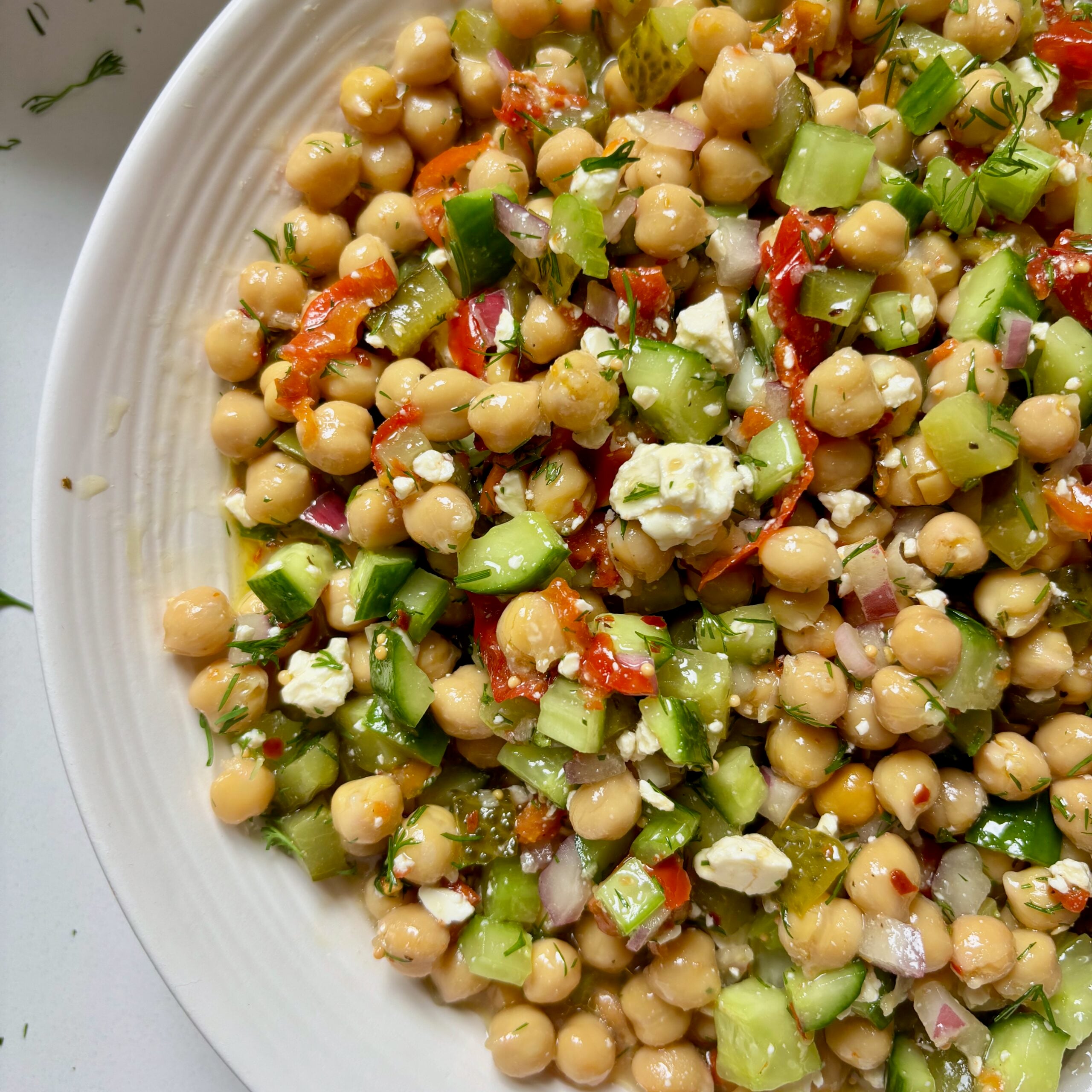 Close-up of marinated chickpea salad with pickles, banana peppers, and feta cheese.