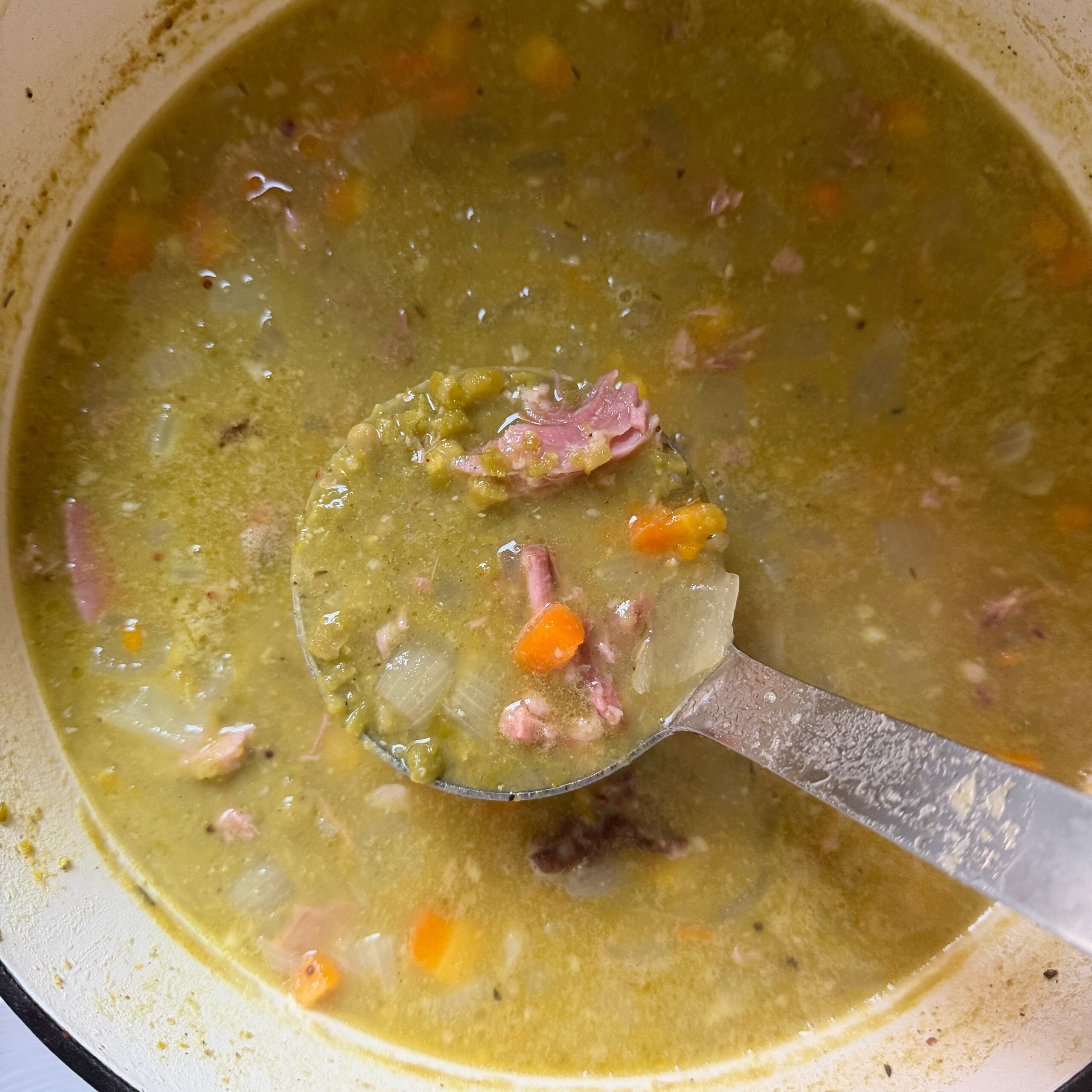 Pot of hearty green split pea soup with carrots, celery, tender ham and a spicy butter topping.